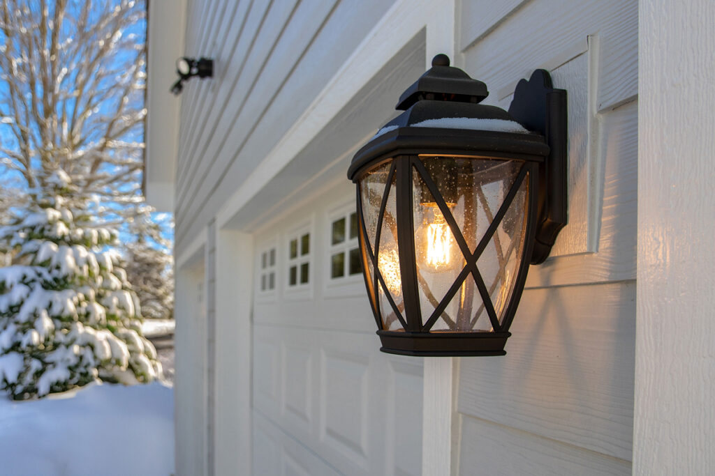 A close up of a garage with a lantern light on the outside during the winter.